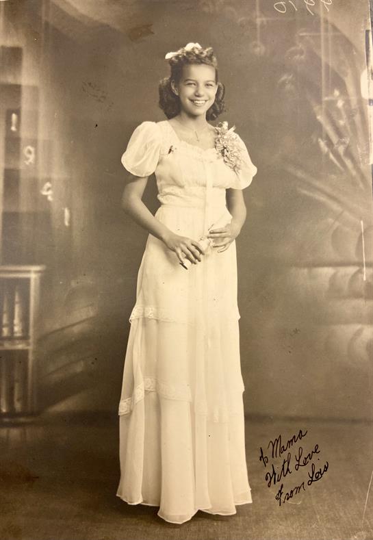A woman is wearing a beautiful vintage gown, smiling in a softly lit studio setting.