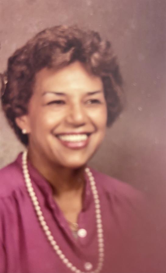 A joyful woman with curly hair and a pearl necklace radiates elegance in a soft portrait.