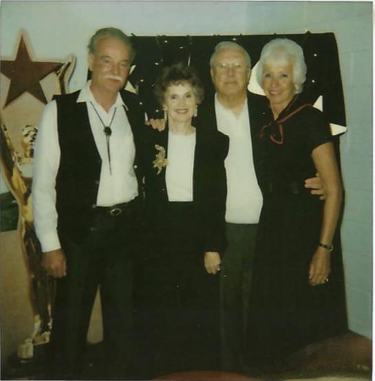 Four friends stand closely together, smiling while wearing casual attire during a fun gathering.