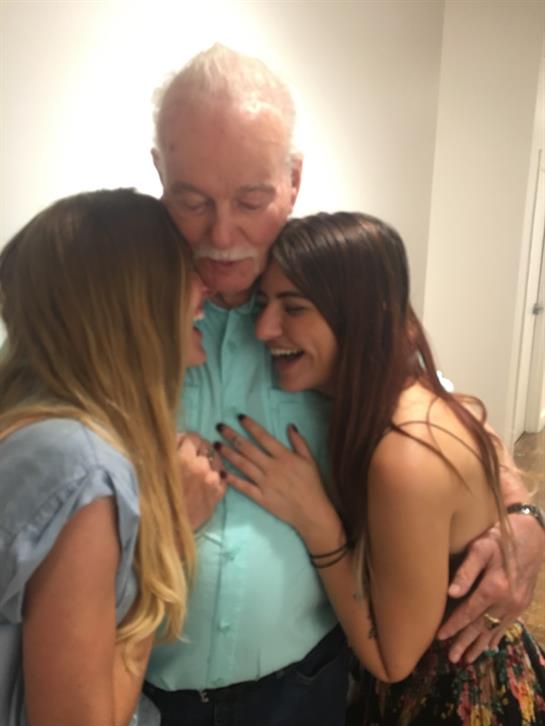 Laughter surrounds two women enjoying a joyful moment with an older man at a family event.