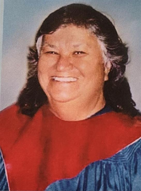Elder woman smiles broadly, dressed in colorful traditional clothing, celebrating cultural heritage.