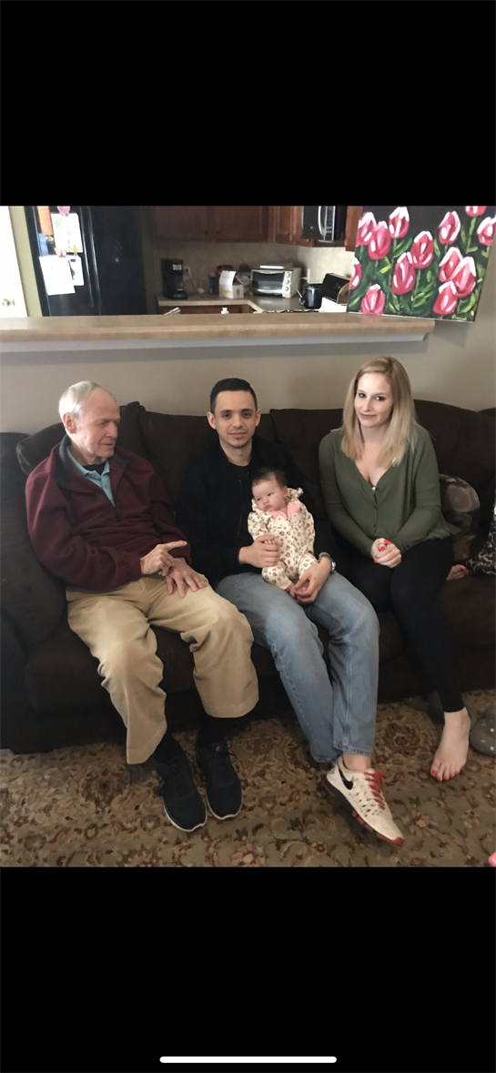 Family members sit together on the couch, sharing smiles and bonding over a newborn baby.