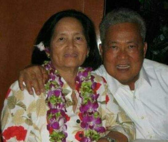 An elderly couple joyfully celebrates their bond in leis at a festive gathering.