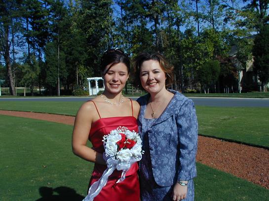 Two friends in formal wear hold a floral bouquet outside under blue skies.