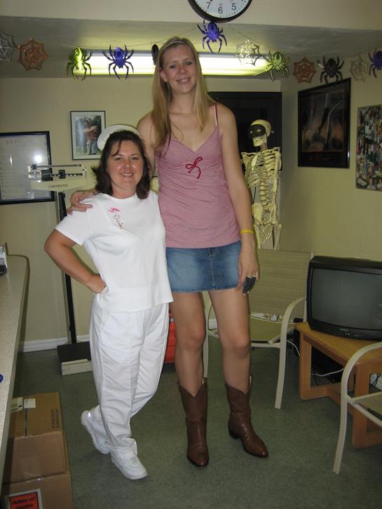 Two women stand side by side, one tall and the other shorter, in a fun and lively indoor space.