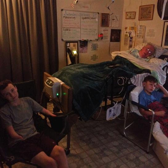 Two people are seated in chairs while another is lying on a bed in a warm, inviting room at night.