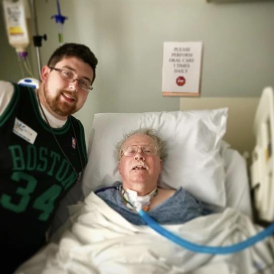 Grandson shares a joyful moment with his grandmother in her hospital room, both smiling happily.