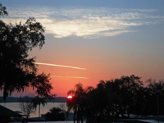 Vibrant sunset paints the sky in orange and pink hues over a calm lake surrounded by trees.