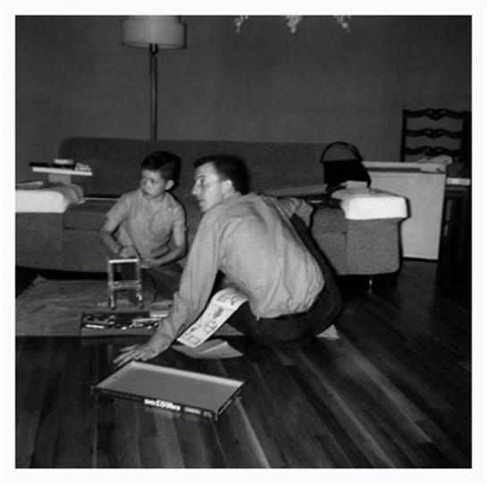 A father and son enjoy quality time together, engaged in a board game on a wooden floor.