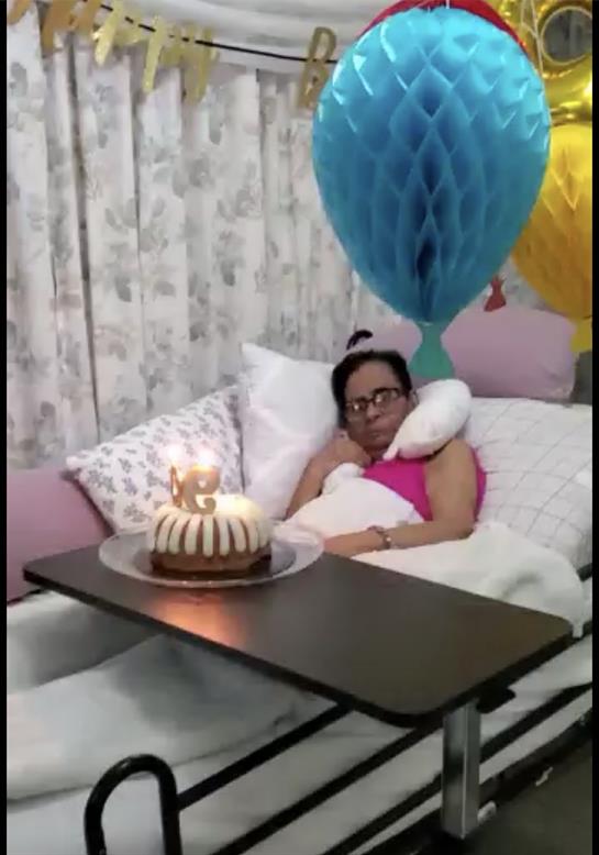 A person in bed celebrates their birthday with a cake, balloons, and a cozy atmosphere.
