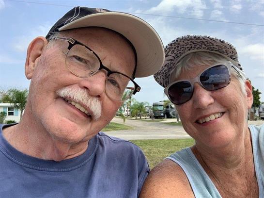 A joyful couple takes a selfie outdoors, enjoying bright sunshine and warm weather.