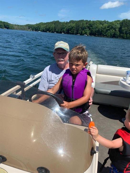 A young boy is steering a boat with family enjoying a sunny day at the lake.