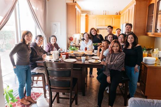 Groups of friends enjoy lively conversation and delicious food in a bright kitchen together.