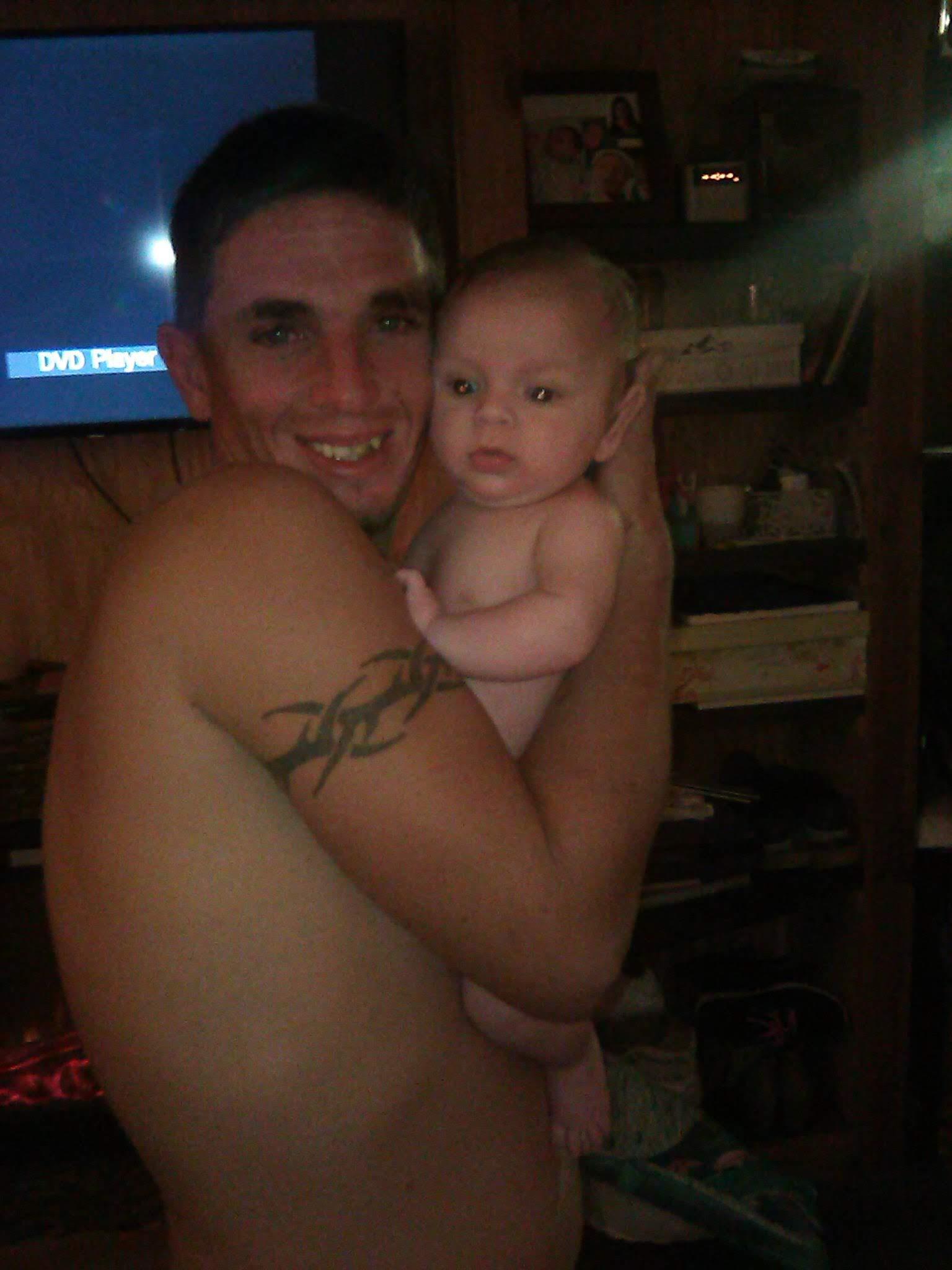 A smiling father holds his baby close in a warm, welcoming room, highlighting their bond.