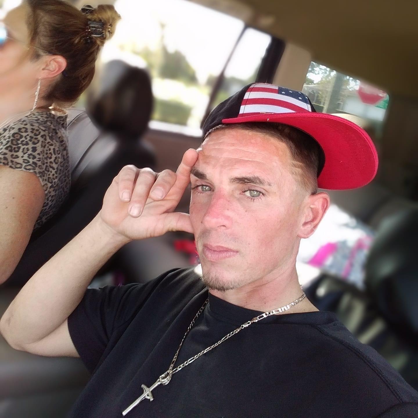 A man makes a fun hand gesture while wearing a red and blue baseball cap.