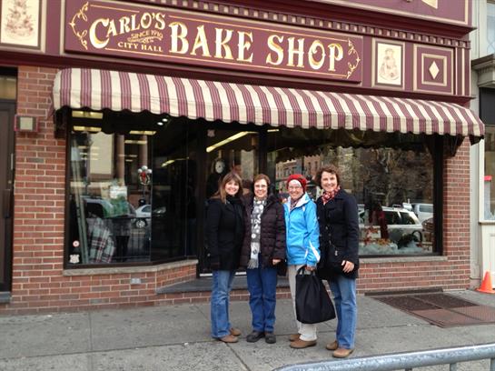Four friends stand in front of a charming bakery, smiling on a chilly day in the city.
