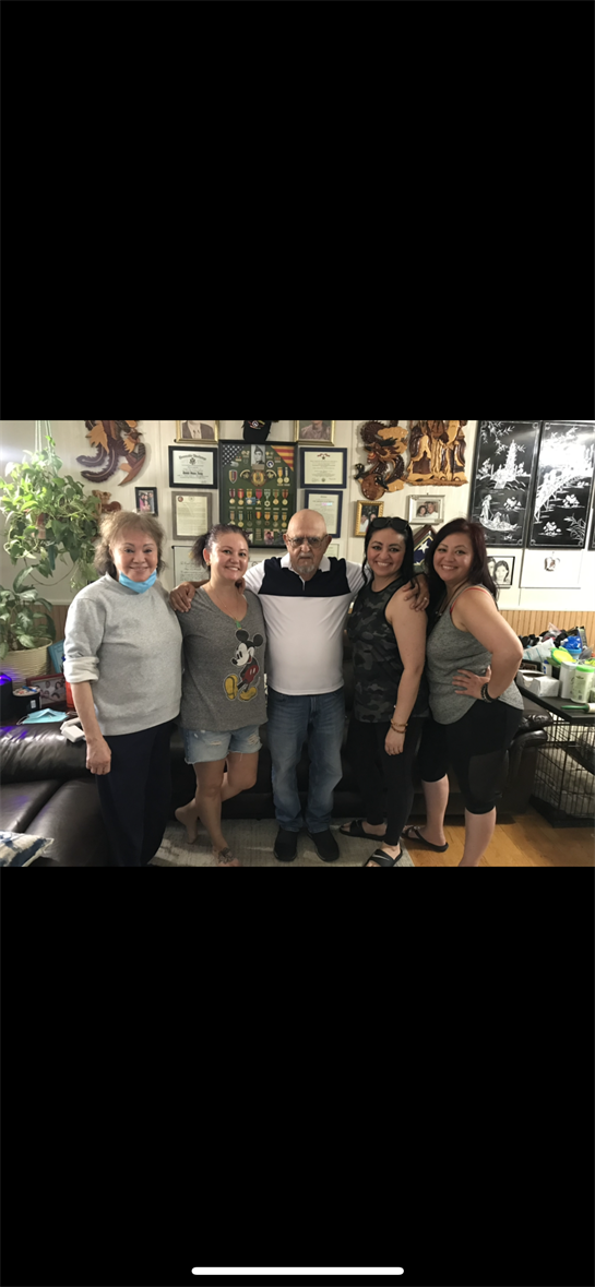 Five family members smiling in a living room filled with personal memorabilia and decorations.