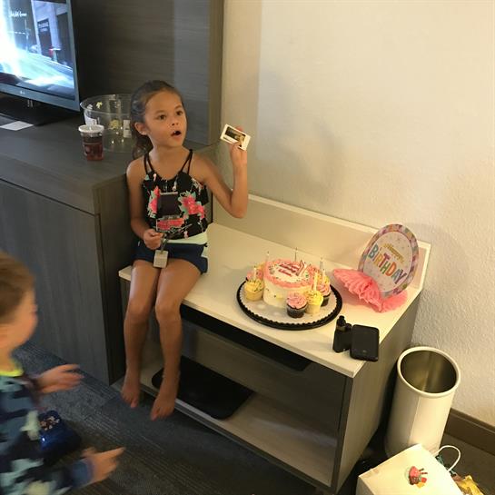 Children are celebrating a birthday with cake and decorations in a cozy hotel room.