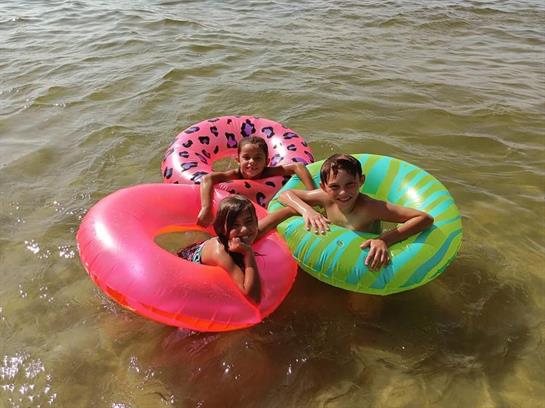 Three children enjoy floating on inflatable rings in warm water under the sun.