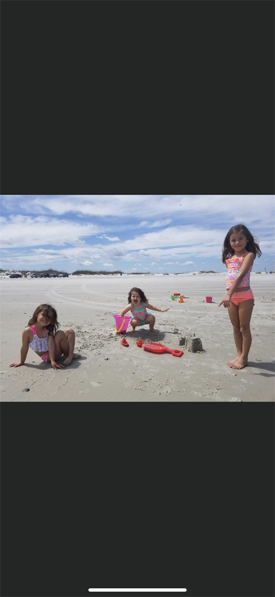 Three young girls play in the sand, crafting sandcastles under a bright sky at the beach.