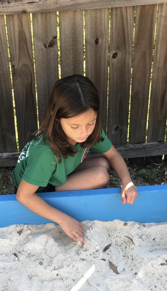 Child focused on building and exploring sand in a blue sandbox in a backyard setting.