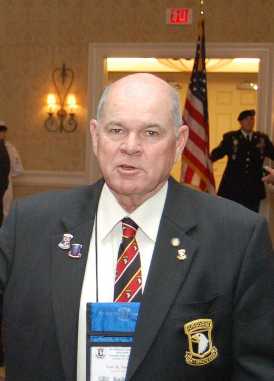 A distinguished elderly man speaks at a formal military gathering, surrounded by attendees.