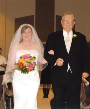 Bride in a white gown walks with her father, holding a vibrant flower bouquet in a festive setting.