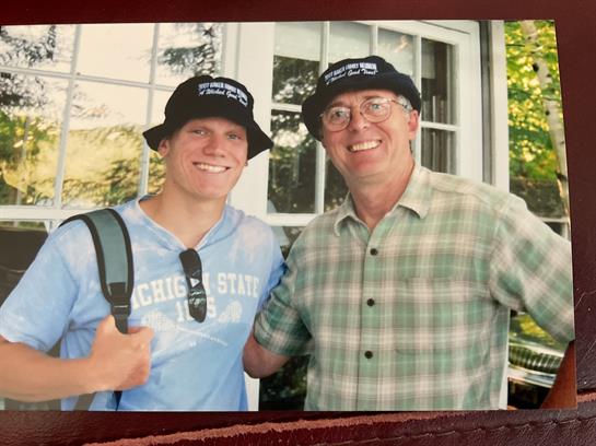 Two men pose happily outdoors with engaging smiles, enjoying a summer day in a relaxed setting.