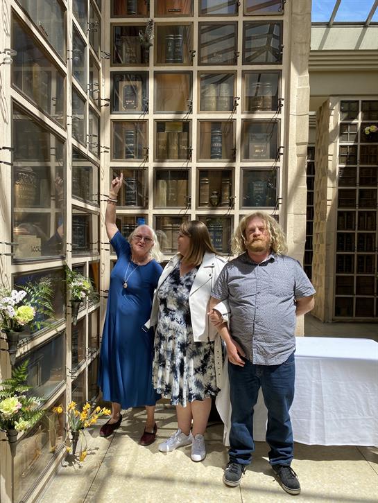 Three people gather at a memorial garden, sharing memories and honoring the lost with flowers.