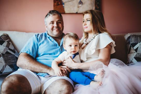 A family shares quality time on the sofa, with the toddler cozy in their arms.