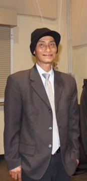 Individual wearing a suit and hat is engaging with others in a casual indoor environment.