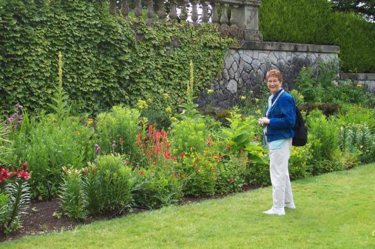 A cheerful woman stands amidst colorful flowers in a beautifully landscaped garden.