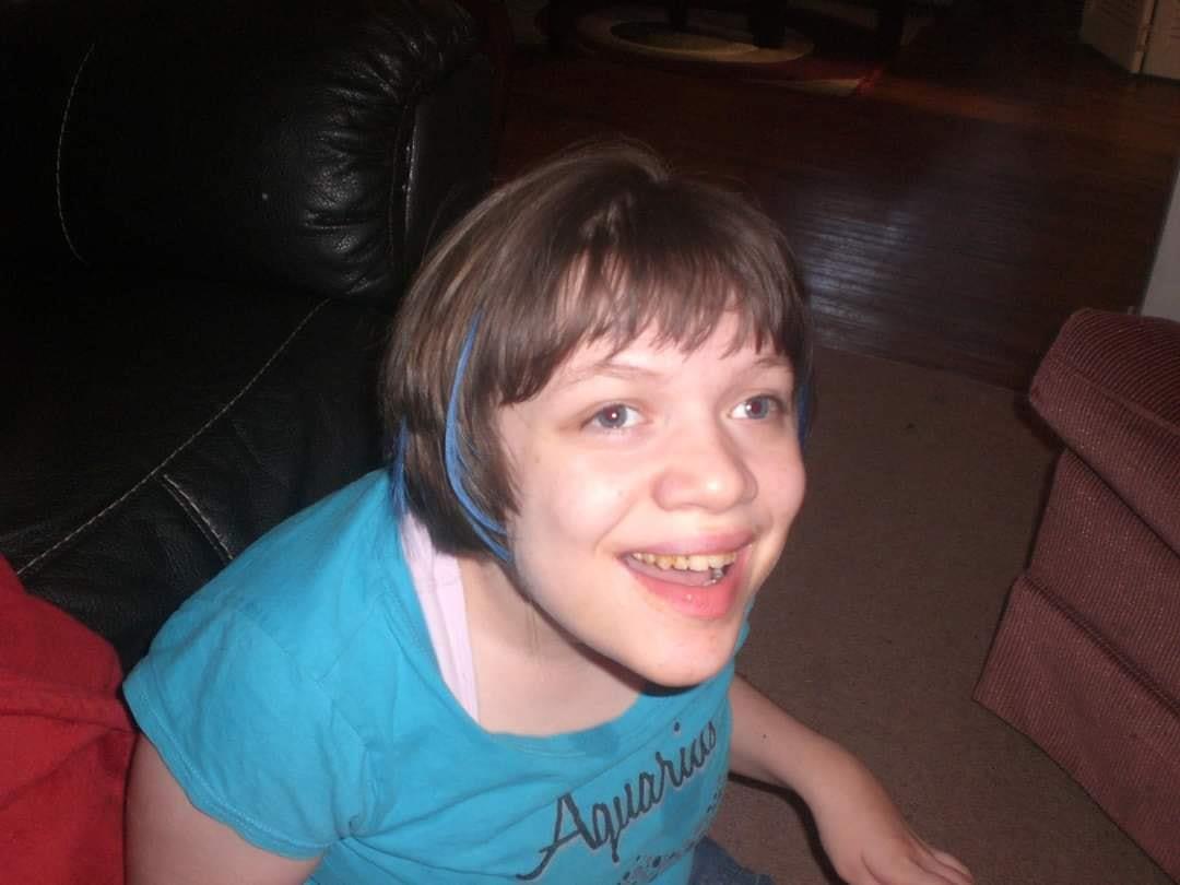 A child with short hair is smiling happily while sitting on a sofa, enjoying time indoors.