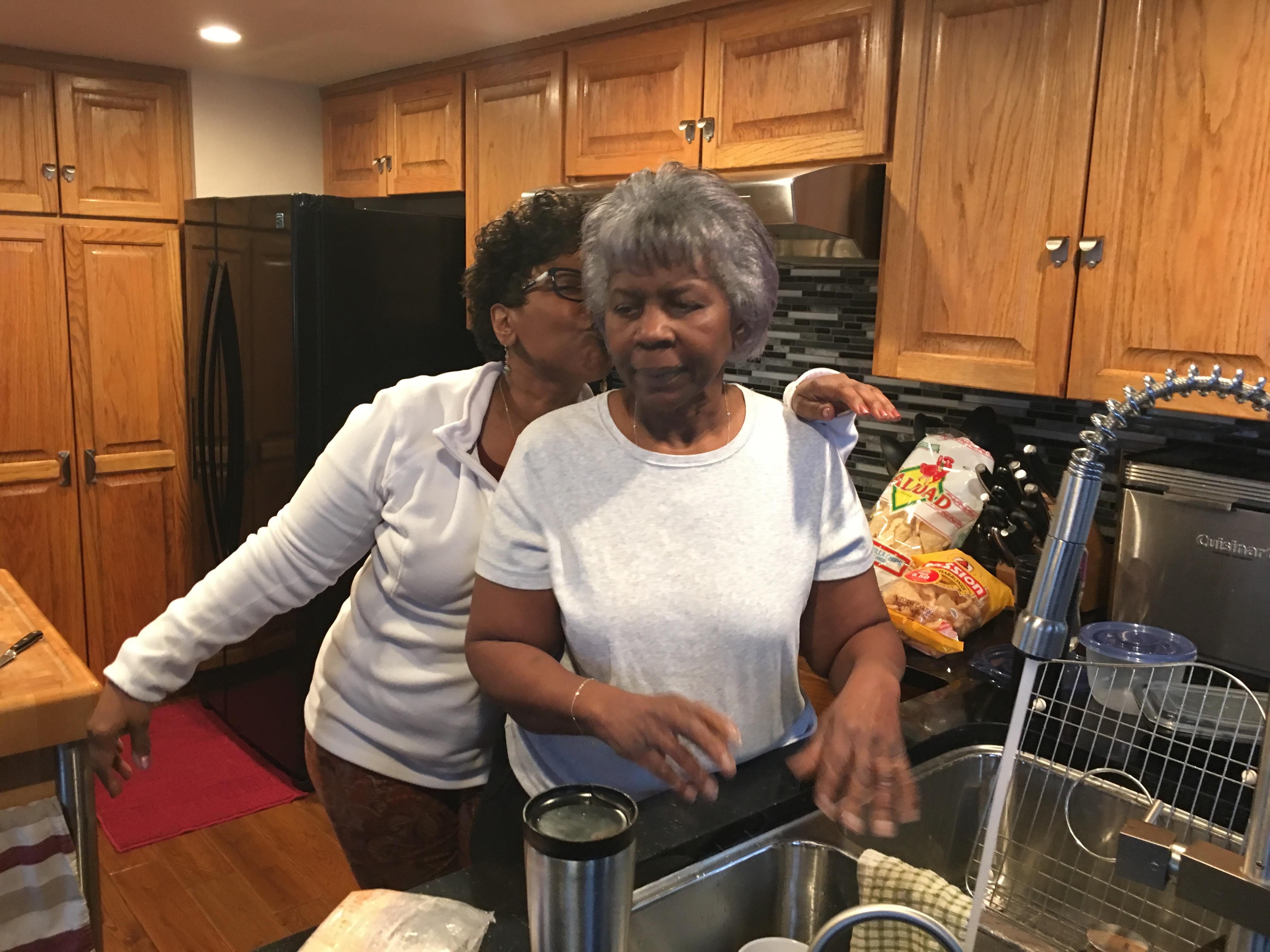 Two women work together in a kitchen, preparing food, surrounded by kitchenware and warmth.