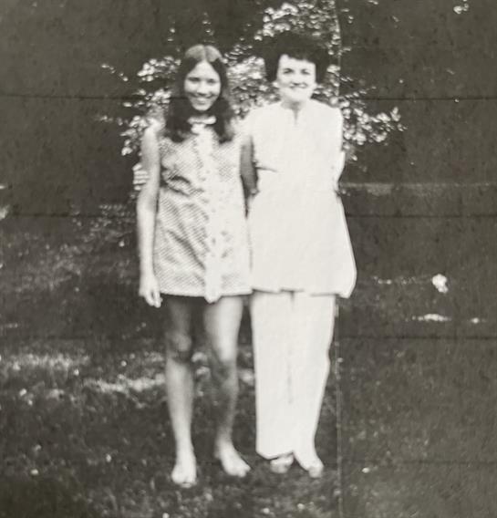 Two individuals pose together in a lush garden, showcasing their casual summer outfits and joy.