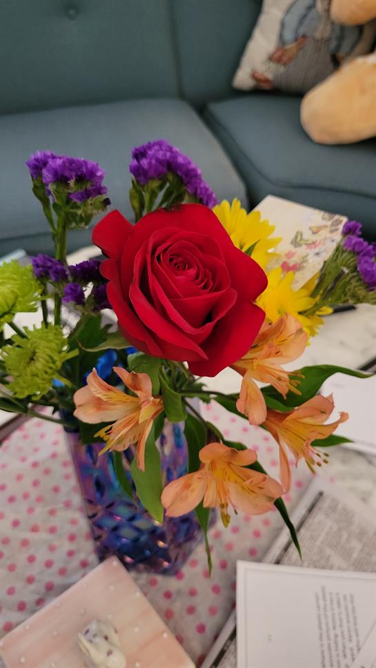 Beautiful bouquet showcases a red rose surrounded by colorful flowers on a table.