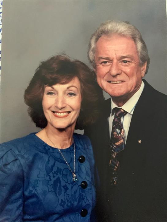 Older couple poses happily, dressed elegantly, capturing a moment of joy at a formal gathering.