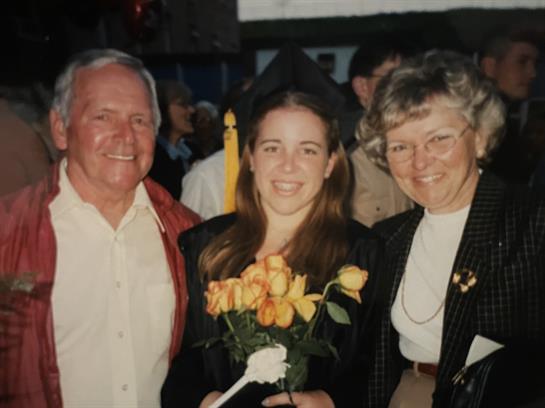 Family members gather around a graduate holding flowers in a joyful outdoor celebration.