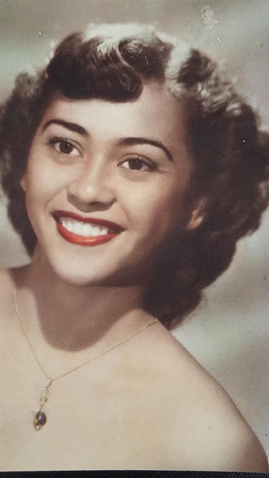Woman with curly hair and red lipstick smiles warmly, embodying classic beauty and charm.