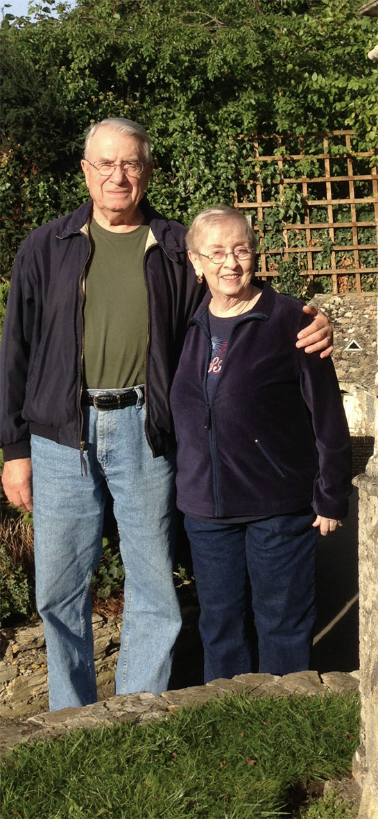 Smiling couple stands together outdoors in a lush setting, enjoying their time in nature.