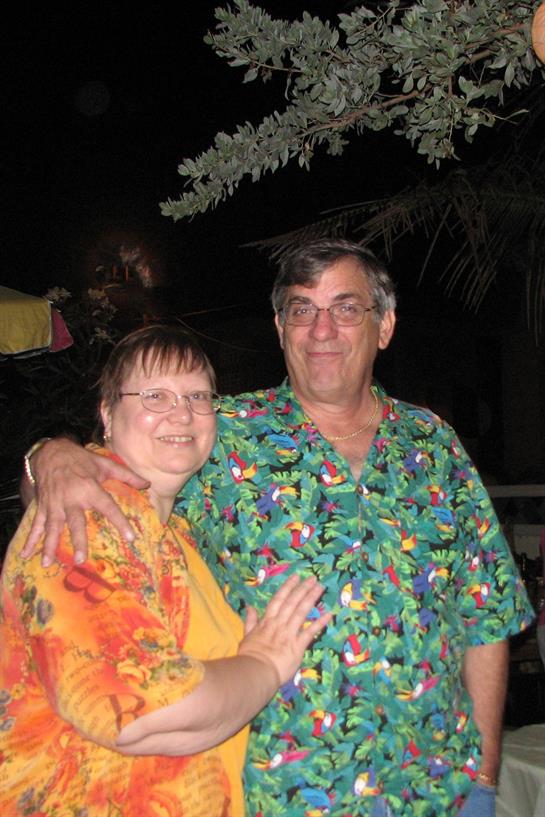 Two people pose happily beneath the night sky, adorned in vibrant tropical attire at a celebration.