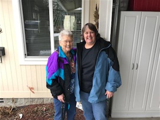 Two women pose happily outside a house, showcasing warmth and friendship in cloudy weather.