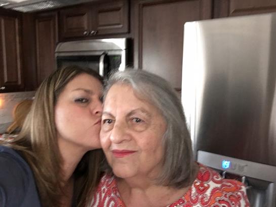 A woman shows love to her grandmother with a sweet kiss in a cozy kitchen setting.