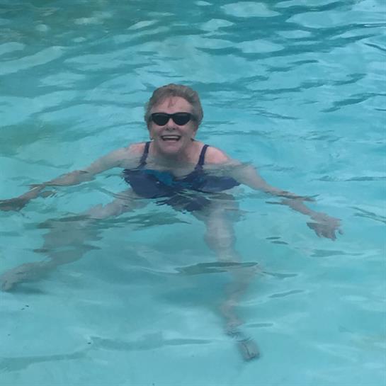 A woman wearing sunglasses swims joyfully in a clear blue pool, enjoying her time outdoors.