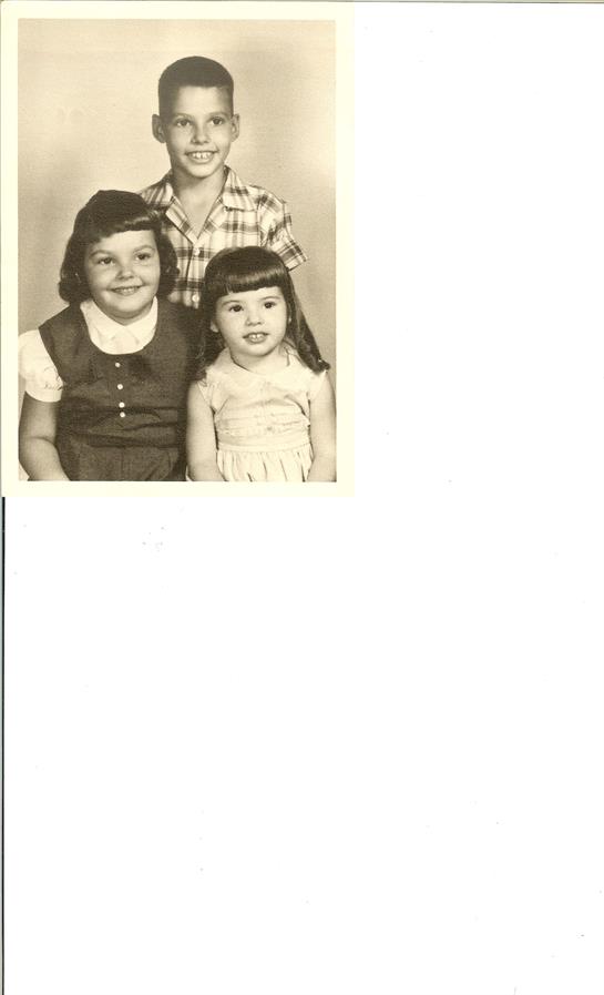 Three young kids smile together in classic 1960s fashion and hairstyles.