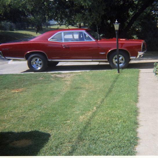A vintage red car stands parked beside a well-maintained lawn on a bright afternoon.
