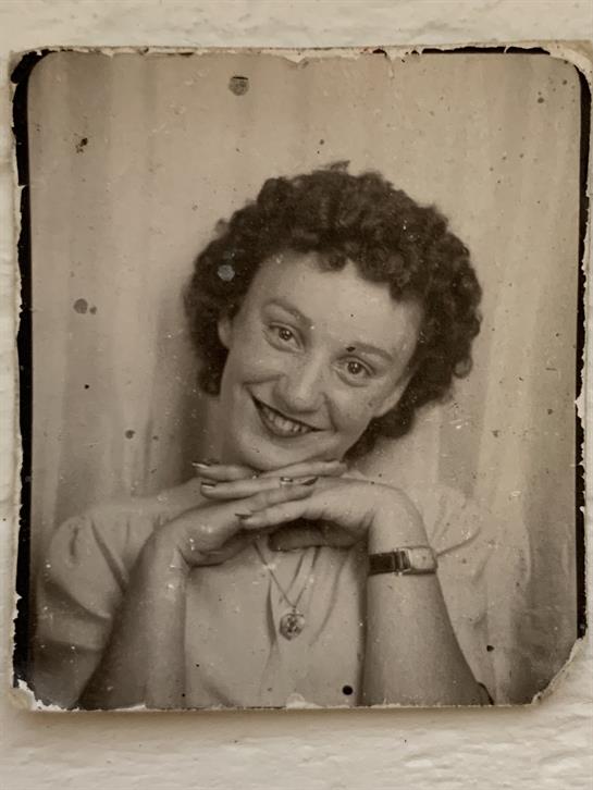 Woman with curly hair poses with a cheerful expression, hands under her chin, in a vintage style.