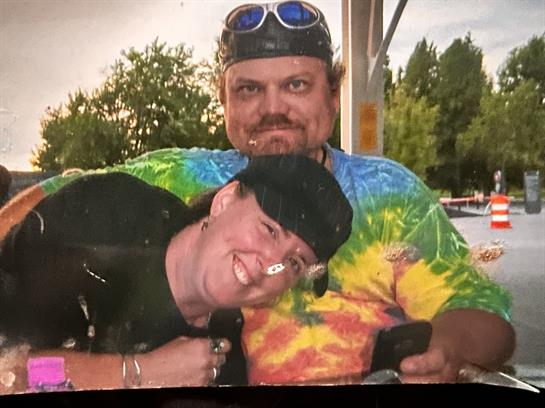 Two individuals embrace joyfully, showcasing bright tie-dye clothing during a sunny day out.