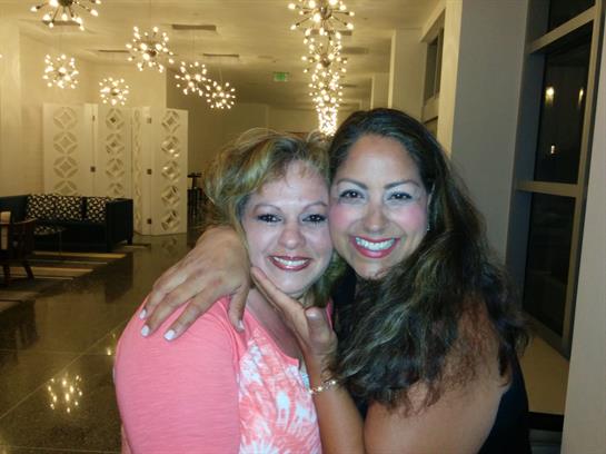 Two women share a joyful moment, smiling and embracing in a beautifully decorated indoor venue.
