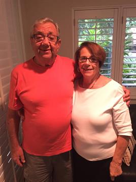 A man and woman stand close together, smiling happily in a well-lit room.